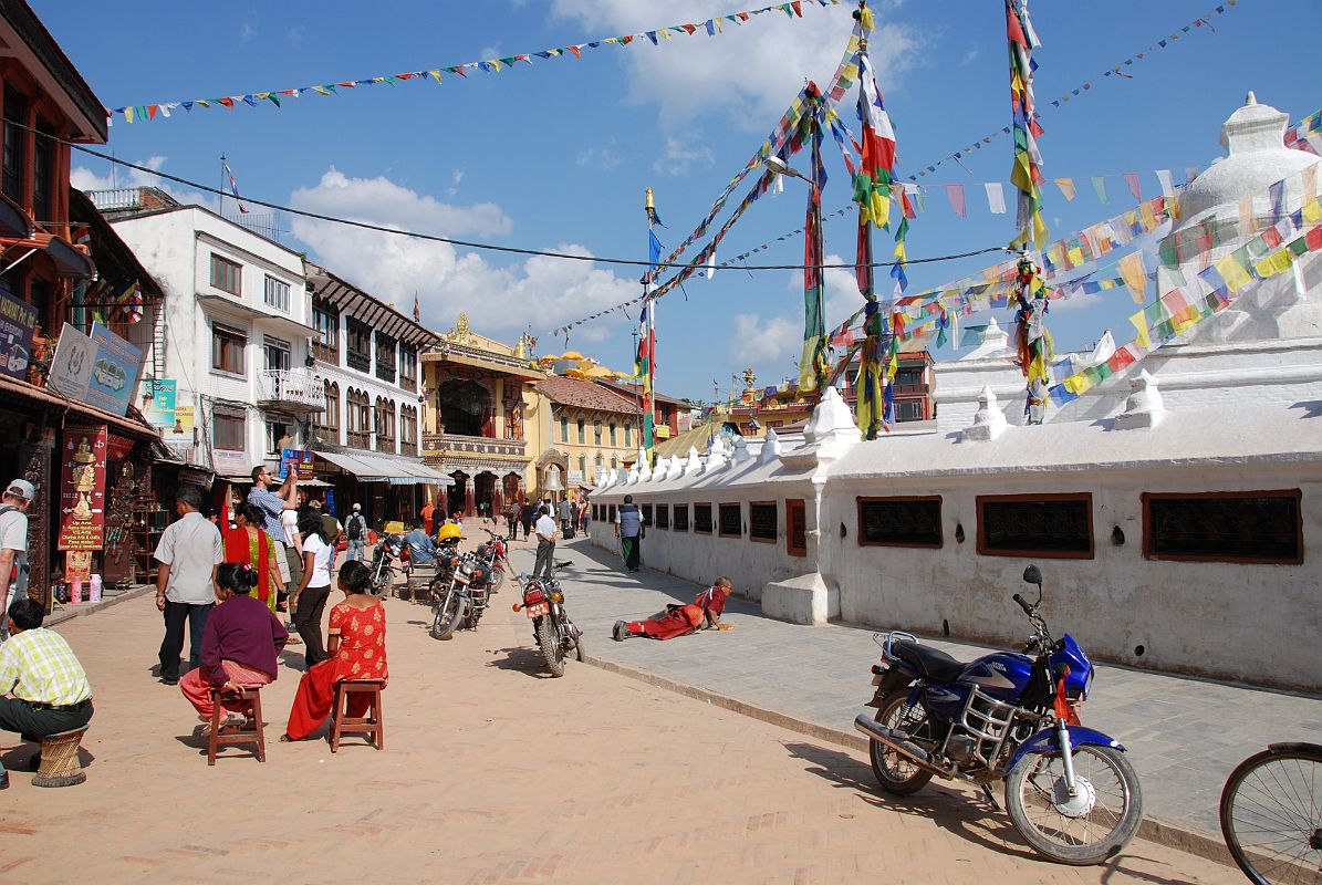 Kathmandu Boudhanath 08 Boudhanath Kora With Shops Circling The Stupa As I turned left to join the throngs of people doing the clockwise Boudhanath Kora, I noticed the Tibetan Buddhist shops, the Jamchen Gompa, and a pilgrim prostrating around the Stupa.